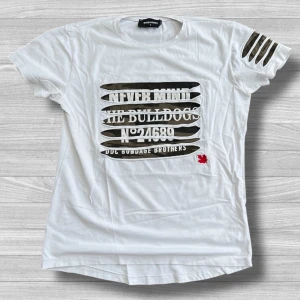 Dsquared2 t-shirt - Cool vit t-shirt från Dsquared2 i bomull med unika slitsar både på bröstet och ena ärmen. Tryck med texten 'Never Mind The Bulldogs' och en liten röd lönnlöv-detalj. Passformen är normal och t-shirten har rund hals och korta ärmar.