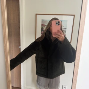 Mörkgrön teddyjacka med hög krage - Säljer en mörkgrön päls jacka  med hög krage och två stora fickor framtill. Jackan har en loose passform och är tillverkad i mjukt, fluffigt syntetmaterial som ger en riktigt mysig vibe. Perfekt för dig som gillar oversized och chill stil.