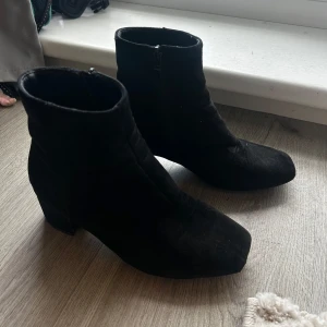 Svarta mocka stövletter med klack - Snygga svarta stövletter i mocka med rund tå och låg klack. Skorna har dragkedja på sidan för enkel påtagning och en stilren, minimalistisk look som passar till många outfits.