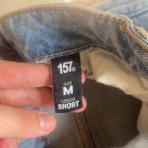 Ljusblå ripped jeans från 157, M - Säljer ett par ljusblå jeans från 157 i storlek M, short längd. Jeansen har klassisk femficksdesign, dragkedja och knapp framtill samt slitna detaljer och hål vid knäna för en cool, avslappnad look. Provade en gång.