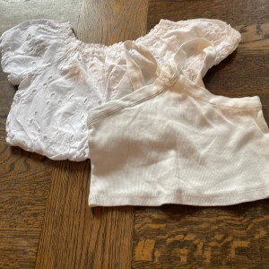 2 vita toppar från Zara, stl 8-9 år - Två vita toppar från Zara. Ena är en ribbad, ärmlös crop top med oneshoulder och liten blomdetalj på axelbandet. Den andra är en romantisk blus med broderade hål och puffiga offshoulder-ärmar. Perfekta för sommarens alla tillfällen!