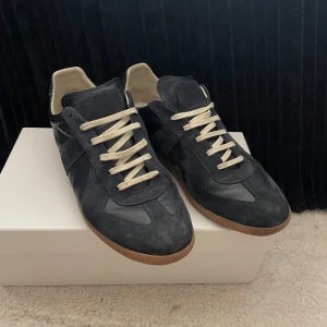  Maison Margiela sneakers i mocka - Snygga mörk blåa sneakers från Maison Margiela med ovandel i mocka och skinn, beige snörning och klassisk gummisula. Skorna har en stilren och tidlös design med rund tå och diskreta detaljer. Bara att skriva vid funderingar . Priset kan diskuteras