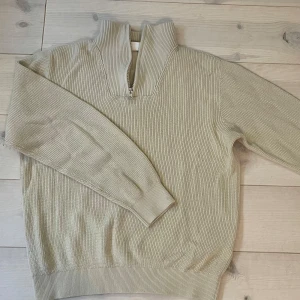 Beige ribbad half zip-tröja Kappahl - Beige ribbstickad tröja från Kappahl med hög krage och half zip-dragkedja. Tröjan har lång ärm och är i ett mjukt, stickat material som känns både stilrent och bekvämt. Perfekt för lager-på-lager och snygg till jeans eller kjol.