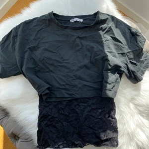 Svart linne och t shirt - Säljer ett svart linne från Kappahl med tunna axelband och v-ringning. Hela linnet är täckt av snygg spets som ger en cool och feminin vibe. Perfekt att styla lager på lager eller bära som det är till jeans eller kjol. Och en cropped t shirt till som är ifrån Zara 