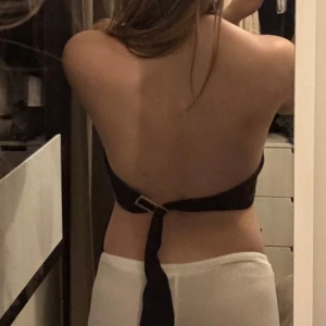 Svart halterneck topp med knyt - Säljer en svart halterneck topp med öppen rygg och knytning bak. Toppen har en hög hals och är ärmlös, vilket ger en snygg och stilren look. Perfekt för dig som gillar minimalistiska plagg med en twist.