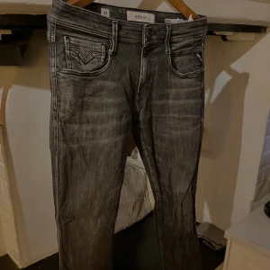 Replay Anbass svarta jeans - Snygga svarta Replay Anbass jeans med slitna detaljer och klassisk femficksdesign. Jeansen har en smal passform och är tillverkade i stretchig denim för extra komfort. Perfekta för dig som gillar en modern och stilren look. Storlek 29:30