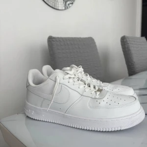 Nike Air Force 1 helvita sneakers - Säljer ett par klassiska Nike Air Force 1 i helvitt skinn. Skorna har lågt skaft, rund tå, snörning och perforerade detaljer framtill för extra ventilation. Perfekta för dig som gillar en clean och tidlös look. Passar till det mesta och är superenkla att matcha.