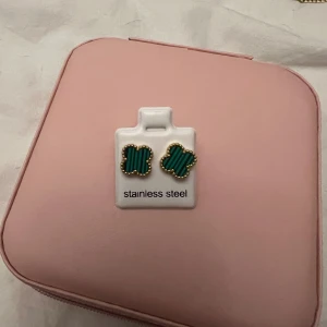 Grönrandiga örhängen i guld - Säljer ett par snygga örhängen i form av fyrklöver med grönrandigt mönster och guldfärgad kant. Tillverkade i rostfritt stål, perfekta för dig som gillar färg och coola detaljer. Passar till alla tillfällen när du vill sticka ut lite extra.