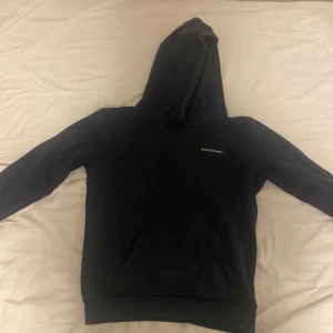 Svart hoodie från Peak Performance - Mörkblå hoodie från Peak Performance med klassisk logga på bröstet. Tröjan har huva, magficka och ribbade muddar. Perfekt för chill dagar eller när du vill ha en enkel och stilren look.