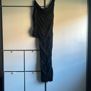 Svart långklänning med oneshoulder - Säljer en svart långklänning med snygg drapering och oneshoulder-design. Klänningen har en lång ärm på ena sidan och är figurnära med coola rynkade detaljer längs hela längden. Perfekt för dig som vill sticka ut med en elegant och modern look.