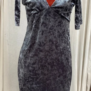 Grå sammetklänning med v-ringning 36 - Grå klänning med v-ringning och knytband på axlarna. Klänningen har en figurnära passform. Saknar tvättråd! Längd: 88 cm Bystvidd: 46 cm. Katter finns i hemmet! 01