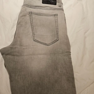 Grå jeansshorts från SMOG, storlek M - Säljer ett par grå jeansshorts från SMOG i storlek M. Klassisk femficksmodell med knapp och dragkedja fram, bälteshällor och snygga kontrastsömmar. Perfekt längd som slutar strax ovanför knäna, passar dig som gillar enkel och clean streetstil.