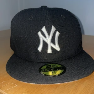 Svart New Era Yankees 59FIFTY keps - Säljer en svart New Era 59FIFTY keps med klassiskt New York Yankees-logo broderat i vitt framtill. Kepsen har platt skärm och MLB-logga baktill. Insidan har märkning och storlekslapp. Perfekt för dig som gillar streetwear och sport.