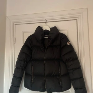 Svart pufferjacka från Colmar - Säljer en svart pufferjacka från Colmar med hög krage. Jackan har en rund Colmar-logga på ärmen och stängs med dragkedja. Perfekt för kalla dagar