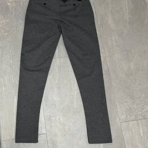 Kostymbyxor  - Snygga grå kostymbyxor från i slim fit-modell. Byxorna har klassisk design med bälteshällor, framfickor och raka ben. Perfekta för en clean och stilren look. Materialet är mjukt och stretchigt för extra komfort.