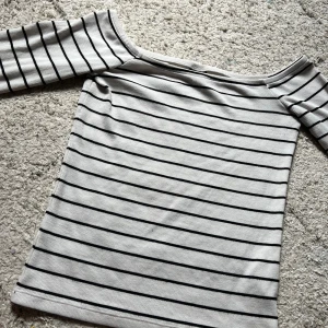 Randig offshoulder topp Gina Tricot - Säljer en vit och svart randig offshoulder topp från Gina Tricot i storlek S. Toppen har trekvartsärm och är ribbad i materialet. Har själv köpt den på en loppis men använt den ca 3 gånger själv.