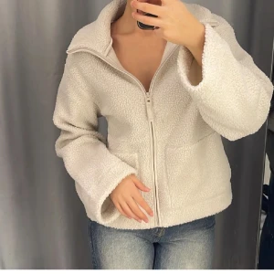 Vit teddyjacka med dragkedja - Mysig vit teddyjacka med stor krage och dragkedja framtill. Perfekt nu till hösten 