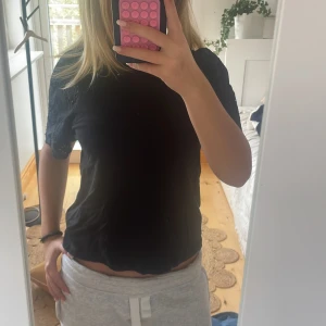 Svart blus med broderade ärmar - Svart blus med korta ärmar och snygga broderade detaljer samt hålmönster på ärmarna. Blusen har en rak passform och är tillverkad i mjuk bomull. Perfekt för dig som gillar stilrena plagg med en twist.