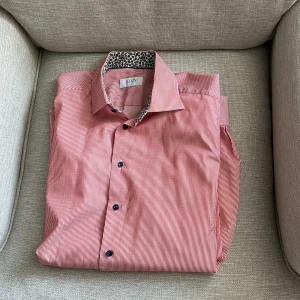 Rödvit randig skjorta från Eton - Snygg rödvit randig skjorta från Eton i slim fit. Skjortan har blommigt mönster på insidan av kragen och svarta knappar framtill. Tillverkad i bomull och passar perfekt för dig som gillar detaljer och stilren design.