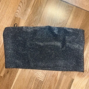 Glittrig silver tubtopp Gina Tricot - Snygg glittrig tubtopp från Gina Tricot i silver. Toppen är axelbandslös och har en bandeau-modell som sitter tight mot kroppen. Perfekt för att sticka ut med sin glittriga yta och coola vibe. Materialet är stretchigt och bekvämt.