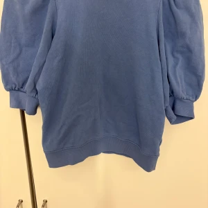 Blå tröja med puffärmar från Lindex - Supersöt blå tröja från Lindex i storlek XS. Tröjan har trendiga puffärmar och ribbade muddar vid ärmslut och nederkant. Perfekt för dig som gillar en chill men ändå snygg stil. Materialet är mjukt och skönt, troligtvis bomullsmix.