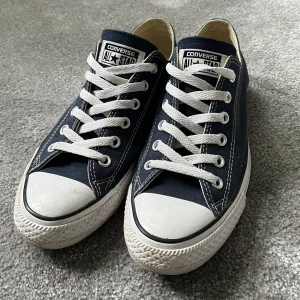 Mörkblå Converse All Star sneakers - Klassiska Converse All Star sneakers i mörkblå canvas med vita gummisulor och tåhättor. Skorna har vit snörning, rund tå och tydliga kontrastsömmar. Perfekta för en avslappnad och cool stil.