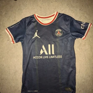 PSG Messi 30 matchtröja Jordan x Nike - Snygg Paris Saint-Germain fotbollströja med Messi 30 på ryggen. Tröjan är marinblå med vita och röda detaljer på krage och ärmslut, PSG-logga på bröstet och Jordan-logga. Tillverkad i lätt, ventilerande polyester med Dri-Fit ADV-teknologi. Perfekt för dig som älskar fotboll och Messi.