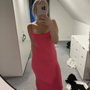 Rosa långklänning med smala axelband - Säljer en snygg rosa långklänning med smala axelband och figurnära passform. Klänningen har en enkel och stilren design som framhäver siluetten. Perfekt för dig som gillar färgstarka och trendiga plagg.