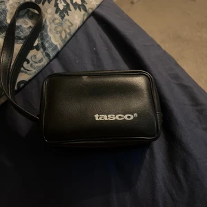 Tasco kikare med väska - Kompakt Tasco kikare med originalväska. Perfekt för natur- och sportaktiviteter. Lätt att bära med handledsrem. Ser ut att vara i gott skick utan synliga skador eller slitage. Levereras med skyddande fodral.