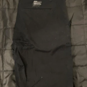 Svarta byxor från Oakley 32W 32L - Svarta byxor från Oakley i regular fit med klassisk rak passform. Byxorna har diskreta fickor och är tillverkade i ett slitstarkt material, perfekta för en clean och sportig look. Passar dig som gillar enkel och stilren design.