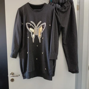 Mörkgrå mjukisbyxor med resårmidja - Mörkgrå mjukisbyxor med resår i midjan, tillverkade i mjukt material. Perfekta för chill dagar och matchar toppen med fjärilspaljetter. Byxorna har en avslappnad passform och är riktigt bekväma.