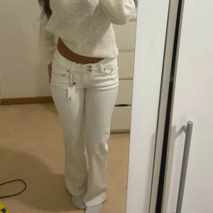 Vita bootcut jeans  - Säljer ett par vita jeans från 157 med snyggt broderi på bakfickorna. Byxorna har bootcut-modell, låg midja och klassisk femficksdesign. Jeansen har dubbla knappar framtill. Perfekta för dig som vill sticka ut lite extra.
