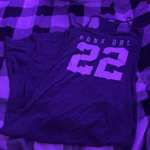 Grå linneklänning BRNX GRL Gina Tricot - Grå linneklänning från Gina Tricot med trycket 'BRNX GRL' och siffran 22 i vitt framtill. Modellen är ärmlös med smala axelband och har en loose passform och sitter väldigt bra och skönt. 