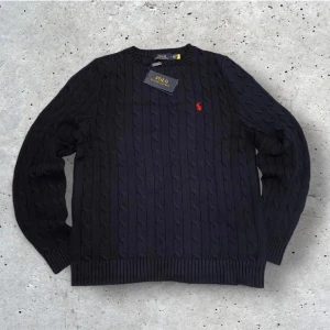 Ralph Lauren Stickad Sweater - Kabelstickad mörkblå tröja från Polo Ralph Lauren med klassisk röd broderad logga på bröstet. Perfekt inför en kall vinter!