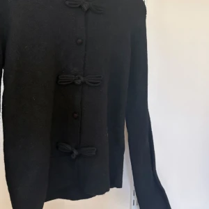 Svart kofta med knyt XS. Oanvänd lappen kvar - Svart kofta med rund hals och dekorativa knyt framtill. Långärmad. Oanvänd lappen kvar.