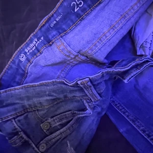 Blå skinny jeans low waist, stl 25 - Snygga blå skinny jeans med låg midja och slitna detaljer. Modellen har klassiska fem fickor, synliga sömmar och en smal passform som sitter tajt längs benen. Perfekt för dig som gillar en modern och avslappnad look.☺️