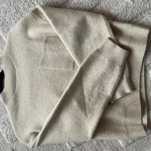 Beige stickad tröja från Zara - Beige stickad tröja från Zara med rund halsringning och ribbade muddar. Tröjan har en liten bröstficka och är i en mjuk, skön kvalitet som passar perfekt till kyligare dagar. Enkel och stilren design som funkar till det mesta.