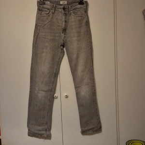 Grå jeans Relaxed Chris 30/34 - Grå jeans i relaxed fit från Relaxed Chris. Modellen har raka ben, klassiska fem fickor och slitna detaljer vid bensluten för en cool, avslappnad look. Jeansen är tillverkade i bomull och har en ljusgrå tvätt.