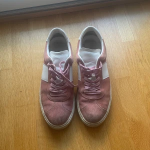 Rosa och vita sneakers från Paul Smith - Säljer ett par snygga sneakers från Paul Smith i rosa mocka med vita skinnpaneler och vita detaljer. Skorna har klassisk rund tå, platt sula och snörning framtill. Perfekta för dig som vill ha en stilren men färgglad look. Nypris va 265 pund (cirka 3400kr). Tyvärr har jag vuxit ur dom därav slumpas dom bort. Sitter lite större än 44, snarare 44,5/45. Kartong och skofodral samt extra skosnöre finns med och kommer självklart medz Tveka inte på att ställa frågor