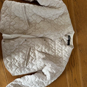 beige jacka från Zara XS - Snygg quiltad jacka från Zara i beige med rund hals och tryckknappar framtill. Jackan har två fickor och ett coolt mönster med hjärtformade quiltningar. Perfekt för dig som gillar stilrena och trendiga plagg.