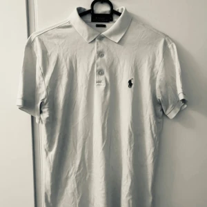 Vit piké från Polo Ralph Lauren S - Klassisk vit pikétröja från Polo Ralph Lauren i slim fit-modell. Tröjan har korta ärmar, krage och tre knappar framtill samt den ikoniska broderade loggan på bröstet. Perfekt till jeans eller shorts för en clean och stilren look.