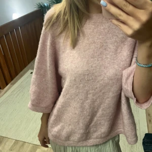 Ljusrosa stickad tröja & Other Stories - Supermjuk ljusrosa stickad tröja från & Other Stories. Tröjan har en avslappnad passform med trekvartsärmar och ribbade detaljer vid halsringningen. Perfekt för lager-på-lager under höst och vinter.