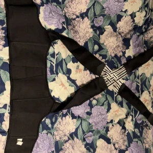 Svart ryggstöd bälte med elastiska band - Säljer ett svart ryggstöd bälte med bred midjedel och elastiska axelband som korsas i ryggen. Bältet har svart och vitt randigt mönster där banden möts och justerbara kardborreband för bästa passform. Perfekt för dig som vill ha extra support under dagen.