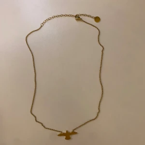 Guldigt halsband - Snyggt halsband med en tunn kedja och ett stilrent fågelhänge. Halsbandet är aldrig använt och därför som nytt.