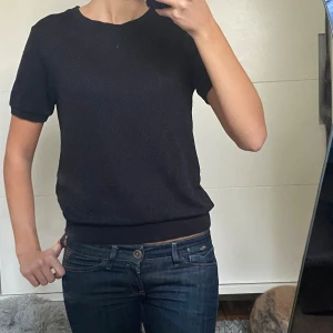 Svart kortärmad tröja med glitter - En svart tröja med korta ärmar och rund hals. Tröjan har en enkel och clean look med ribbade muddar i ärmslut och nederkant. Den år lite lätt glittrig som man ser på bilderna, passar till vardags men också lite finare tillfällen! 