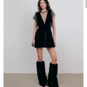Svart fin Klänning från Ida Sjöstedt  - Supersöt svart kortklänning från Ida Sjöstedt med transparent mesh upptill, prickigt mönster och djup v-ringning. Klänningen har volanger längs axlar och urringning samt flera lager tyll för extra volym. Perfekt för dig som vill sticka ut!