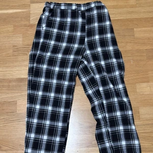 Svarta rutiga byxor från Romwe XS - Svart/vita rutiga byxor från Romwe i storlek XS. Byxorna har elastisk midja och raka ben, perfekta för en chill och avslappnad stil. Tillverkade i mjukt material som känns skönt mot huden.