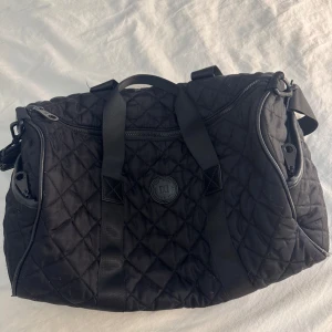 Svart väska  - Svart väska med rymligt huvudfack, flera dragkedjor och praktiska handtag samt axelrem. Väskan har ett stilrent rutmönster.