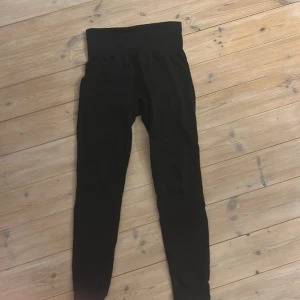 Svarta leggings med hög midja - Svarta leggings med bred, ribbad hög midja och scrunch-detalj bak. Tight passform och stretchigt material som sitter skönt på kroppen. Perfekta för träning eller chill. Klassisk look utan synliga loggor.