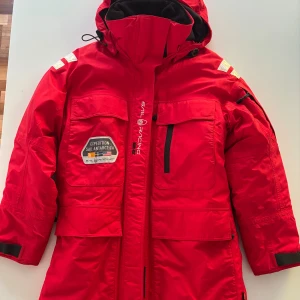 Dunjacka Sail Racing vinterjacka med huva - Glacier Parka dunjacka från Sail Racing med Expedition Sail Antarctica-patch, stora fickor och justerbar huva. Vind- & vattentät med YKK vatten resistent blixtlås som täcker sömmar. Svarta detaljer och reflekterande partier på axlarna. Perfekt för kalla dagar när du vill sticka ut.